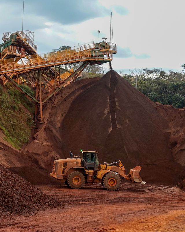 Pá-carregadeira da Lenarge despejando minério na pilha, com correia transportadora ao fundo